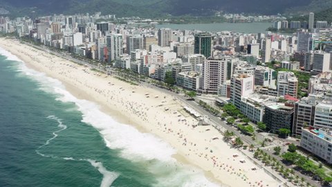 Aerial view of Rio de Janeiro beach. The waters of the Atlantic Ocean wash the sandy beach with umbrellas in the center of the city with high-rise streets and mountains.