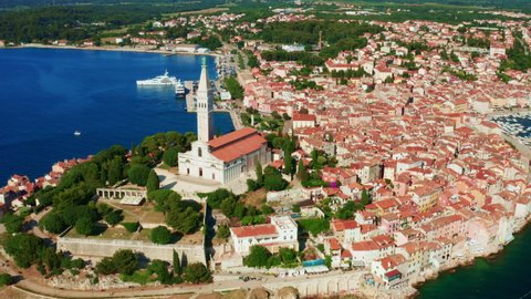 Old town Rovinj with small red roofed houses located near blue Adriatic sea. Church of St. Euphemia in Croatian city on sunny day. Aerial view
