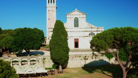 Church of St. Euphemia with bell tower among trees in Rovinj on sunny summer day under blue sky. Old European town with historical architecture. Aerial view