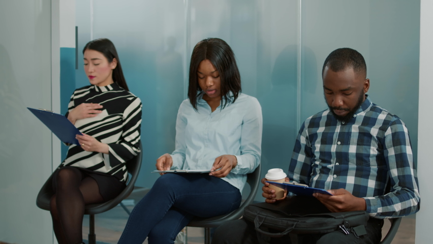 Multiethnic group of candidates waiting to start job interview meeting, sitting in queue with cv. Job applicants preparing for recruitment selection and stressful discussion with hr people.