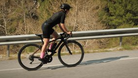 Fit sportive woman climbing up on road bicycle through mountain hill. Professional cyclist training on bike, doing cardio intense workout. Hard workout exercises on bike. Cycling training