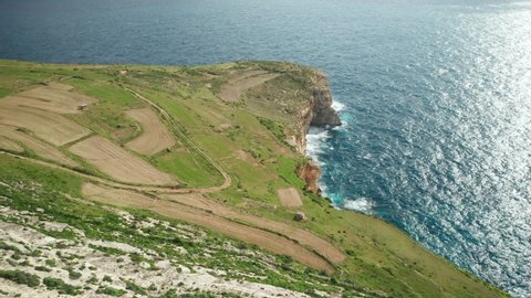 AERIAL: Greenery Plains of Ta Cenc Cliffs near Blue Mediterranean Sea on Windy Day