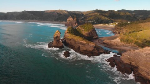 High waves wash the cliffs of the Piha beach which are painted in warm colors at the golden hour