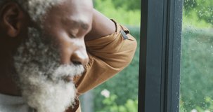 Video of sad african american senior man looking out the window. retirement lifestyle, spending time alone at home concept digitally generated video.