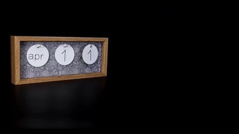 A wooden calendar block showing the date April 11th with a mans hand putting on and taking off the metal discs with the date and month on them, filmed in 8k quality.