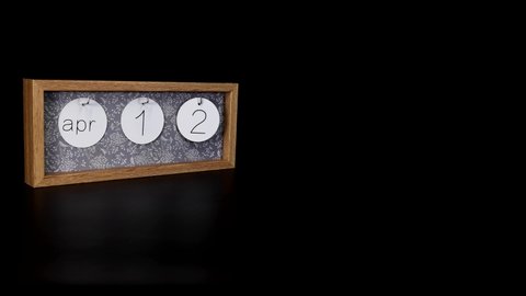 A wooden calendar block showing the date April 12th with a mans hand putting on and taking off the metal discs with the date and month on them, filmed in 8k quality.