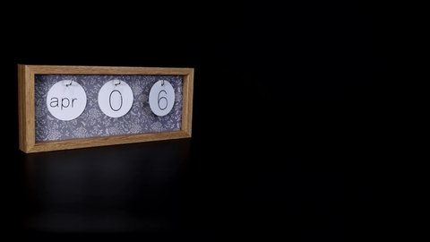 A wooden calendar block showing the date April 6th with a mans hand putting on and taking off the metal discs with the date and month on them, filmed in 8k quality.