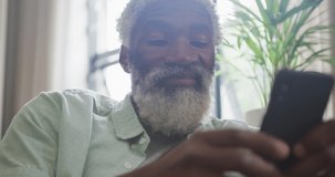 Video of african american senior man using smartphone. retirement lifestyle, spending time alone at home concept digitally generated video.
