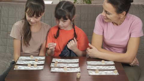 Play lotto game. A pretty mother with her smart children play lotto on the table.