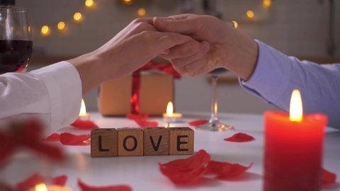 A couple of people in love move the letters and add the word love. Lovers hold hands romantic setting candles wine gifts.
