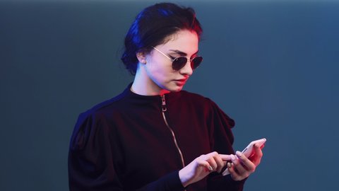 Phone conversation. Sassy girl. Modern gadget. Millennial lifestyle. Cheeky glamorous woman in red neon light talking on cellphone on blue copy space.