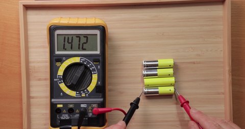 Testing AA battery cells with digital multimeter tool, voltage check showing low value, battery is used and mostly discharged