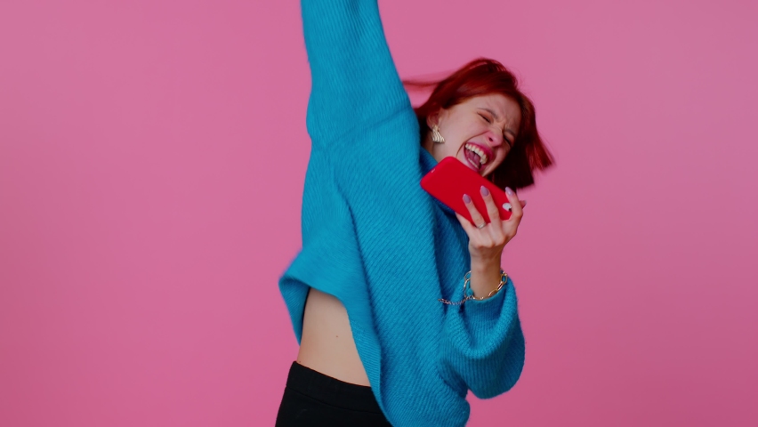 Worried funny addicted woman enthusiastically playing racing video games on mobile phone. Young adult teen girl using smartphone gadget app with drive simulator isolayed on pink studio wall background