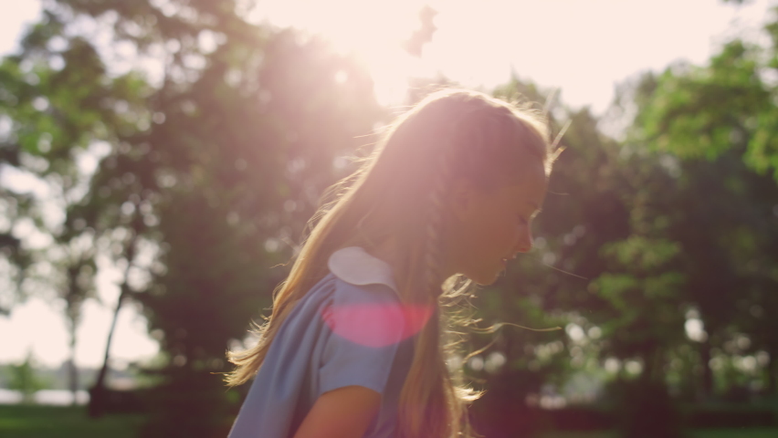 Cute joyful girl picking up hit shuttlecock with racket in golden sunlight. Cheerful pretty kid play badminton in summer city garden. Child have fun on vacation. Family weekend activities concept.