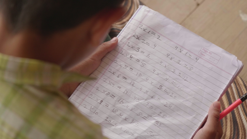 Overhead shot of studying Indian Asian Village little Boy in primary School uniform holding a Notebook in hands with Mathematical Tables of 2 and 4 written on it. Rural Education or child literacy Royalty-Free Stock Footage #1087188344