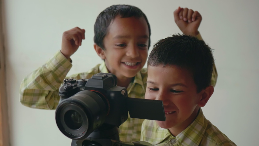 Two young cute smiling Indian male kids or school children are playing with or self-learning how to operate a digital photography camera or DSLR in an interior setup. Concept of Practical education | Shutterstock HD Video #1087188350