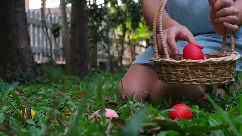 Teen girl collects Easter eggs in a basket in the backyard