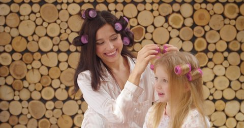 Woman and her little daughter using hair curlers at home