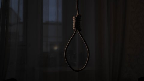 A rope noose hangs in a dark apartment. The concept of personality crisis and suicide.