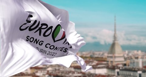 Turin, Italy, January 2022: the white flag with the Eurovision Song Contest 2022 logo waving in the wind with blurred landscape of Turin. The 2022 edition will take place in Italy from 10 to 14 May