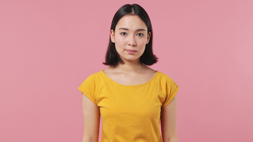Confused shy shamed young woman of Asian ethnicity 20s wear yellow t-shirt look camera spreading hands say oops ouch oh omg i am so sorry isolated on plain pastel light pink background studio portrait Royalty-Free Stock Footage #1087198568