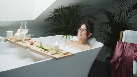 Woman Blowing Foam In Luxury Bathroom In Slow Motion. Girl Taking A Bath. Sexy Woman Bathing With Candles And Relaxing In Bathtub At Home, Having Fun With Foam. Concept Of Beauty, Pampering, Home Spa