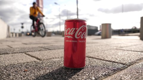WROCLAW, POLAND - FEB 18, 2022: Passing by bicycle cyclist rides near a coca cola can as a trash left on the sidewalk