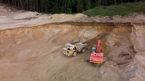 Radashkovchi, Belarus - June 15, 2021. Aerial video coming closer to yellow digger loading extra large truck with sand in sandpit. 