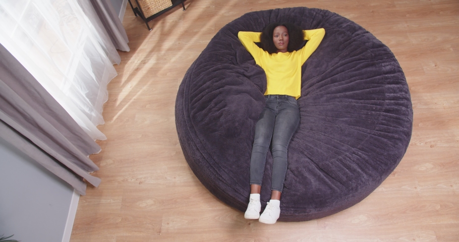 Top view shot of african american wooman lying on sofa with arms crossed behing her head looking onto ceiling. Tired female after work resting. Concept of rest, carefree. Slow motion video.