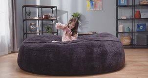 Little girl on sofa with smartphone in her hands. Child playing with gadgets. Girl after school resting on sofa with phone games. Slow motion video.