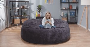 Full size front view portrait of caucasian woman on sofa with smartphone in her hands. Female scrolling social media on gadget. Woman after work resting on sofa with phone. Slow motion video.