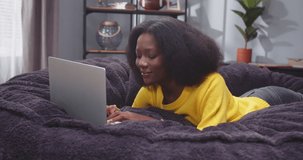 Close up portrait of grown up african american woman lying on sofa with laptop. Female scrolling social media on gadget. Lady after work resting on sofa with computer. Slow motion video.