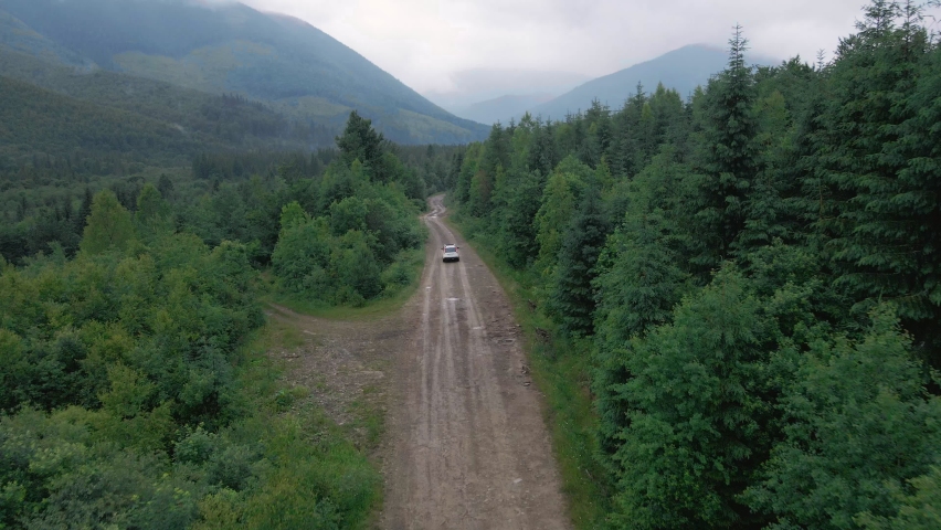 aerial view of suv car moving by path road in mountains overcast misty rainy weather tracking dolly shoot