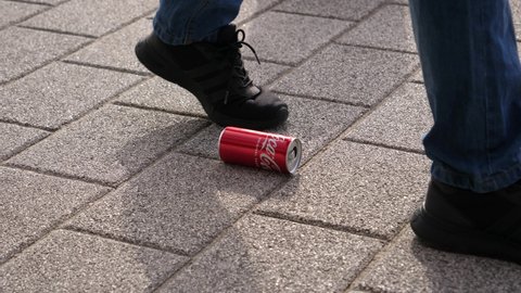 WROCLAW, POLAND - FEB 18, 2022: Man legs walking passing by a coca cola can as a trash left on the sidewalk pavement