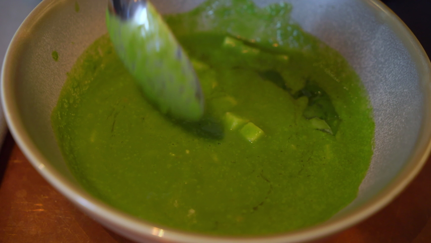 A young woman stirs soup with a spoon. A girl in a restaurant or cafe eats lunch or dinner. Vegetable Italian minestrone soup, green. Tasty meal in Italy. Female takes spoon from napkin.