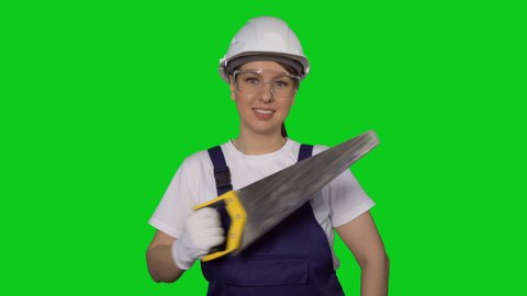 Construction worker. Woman builder in blue overalls and white hard hat hold hand saw. Building, repair and renovation of house or apartment. Female in helmet on green background chroma key.
