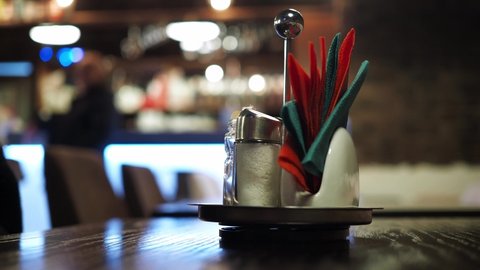 a stand with napkins on the table in a cafe with a blurred bokeh. the people in the background at the bar are blurry bokeh. unrecognizable silhouettes of people in the background