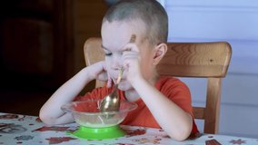 Five years old boy sitting on chair in a kitchen and eating the soup with the spoon. 4k real time video footage