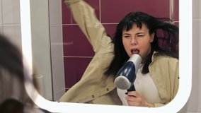 Funny woman in the bathroom dancing and emotionally singing using the hair dryer as a microphone in front of the mirror. Getting ready at home, music concept. - Powered by Shutterstock - Get 15% off with code: PIKWIZARD15