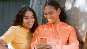 Two beautiful, happy, smiling African American biracial girls teenagers young women outdoors in the city using a smartphone or cell phone for social media or text messaging - Powered by Shutterstock - Get 15% off with code: PIKWIZARD15