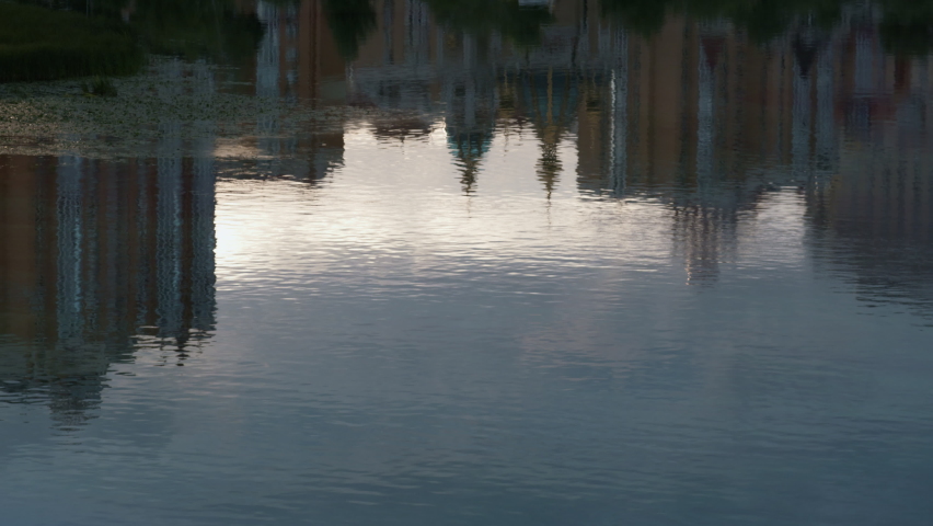 Cityscape buildings reflecting water drone shot. Silent river flowing slow. Abstract multi-storey city architecture residential area sky mirror in calm waterway. Blurry glare on blue turquoise surface - Powered by Shutterstock - Get 15% off with code: PIKWIZARD15