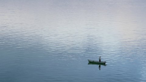 Fisherman standing in boat watching river flow drone shot. Glowing water surface. Unknown man sailor enjoying beautiful relaxing waterway scenery. Calm glaring expanse of blue watercourse lake concept