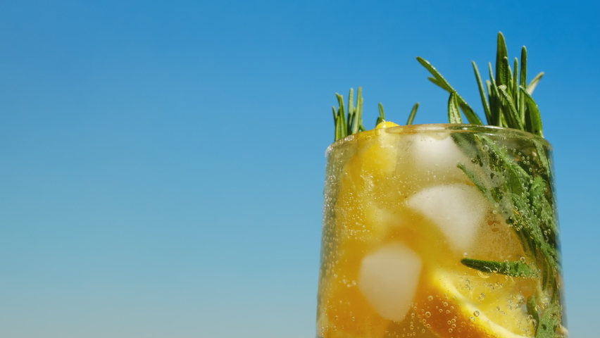 Low alcoholic summer drink. Glass of hard seltzer cocktail with citrus slices and rosemary, blue sea on background. Epic point of view, copy space. 