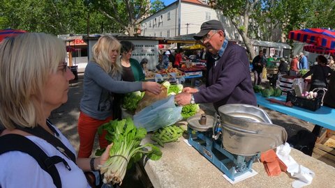 Split, Croatia 10 May 2019 : Blonde tourist woman buying spinach at traditional Croatian vegetable market. Vendor weighing with weights on scale