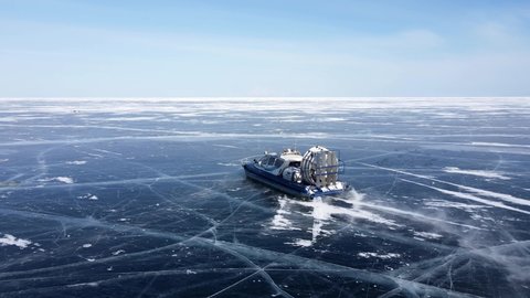 Hovercraft ship rides on clear cracked blue ice. Winter lake Baikal. Natural landscape Siberia Russia.