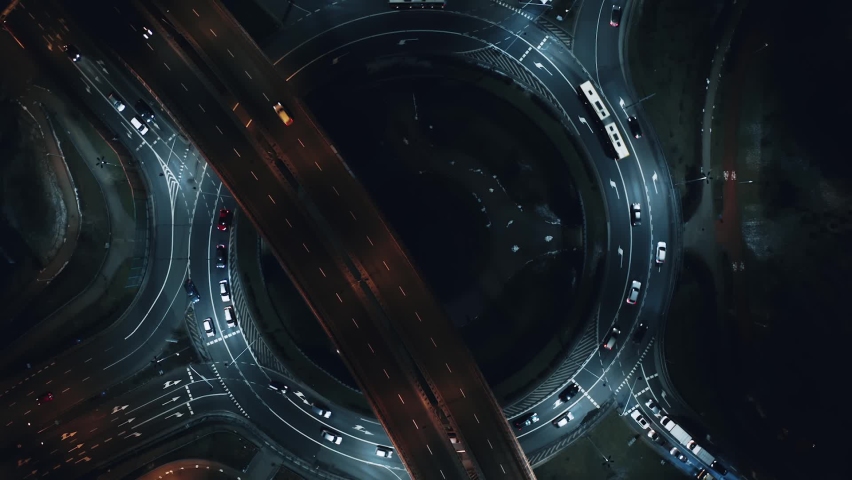 Aerial flyover car traffic roundabout interchange road at night, drone shot top down view expressway intersection in modern city in evening. Cars driving busy junction highway transportation Royalty-Free Stock Footage #1087231574