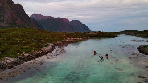 Aerial view in front of kayaks in shallow waters in middle of mountains of Lofoten, Norway - circling, drone shot