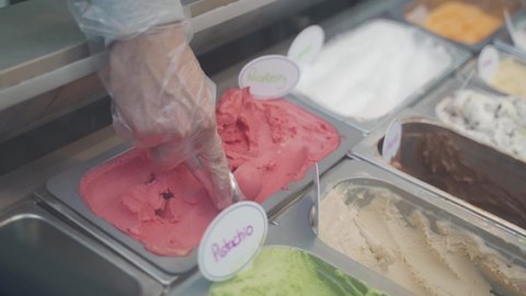 Scooping raspberry gelato with a scooper and close-up of gelato display case