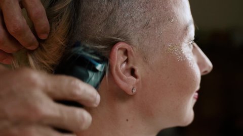 A close-up of a woman's head is shaved bald with a hair clipper indoor.