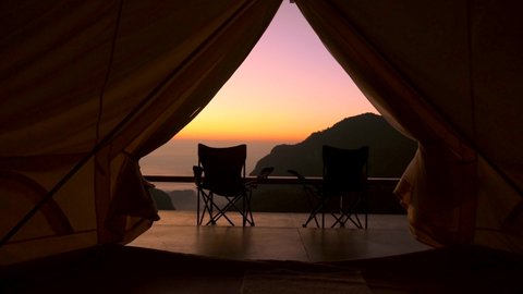 View from tent camping or glamping entrance on amazing sunrise with mountains and two folding camping chair on terrace. Looking through opening door of modern tent. Travel vacation on nature Stock Video